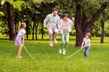 Photo of charming funky family dressed casual outfit playing jumping rope smiling outside urban...