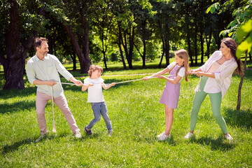 Fototapeta premium Photo of cute charming family dressed casual outfit playing tugging rope smiling outside urban city street