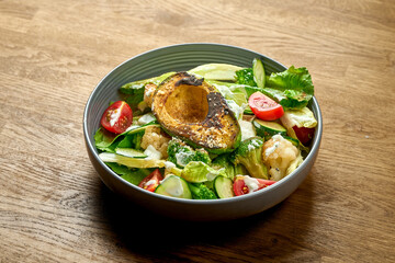 Diet salad with grilled avocado, white sauce and vegetables in a bowl on a wooden background