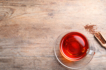 Freshly brewed rooibos tea and dry leaves on wooden table, flat lay. Space for text