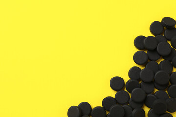 Activated charcoal pills on yellow background, flat lay with space for text. Potent sorbent