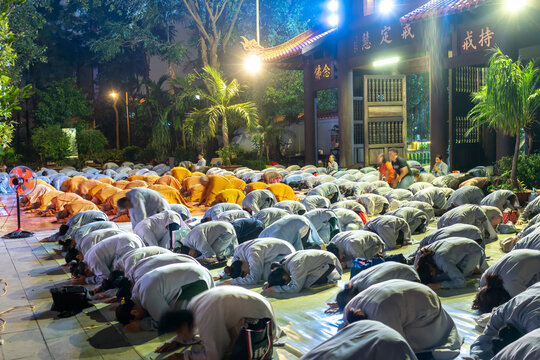 Monks and Buddhists are reverently bowing to Buddha during evening ceremony for Amitabha Buddha at an ancient temple in Ho Chi Minh City, Vietnam