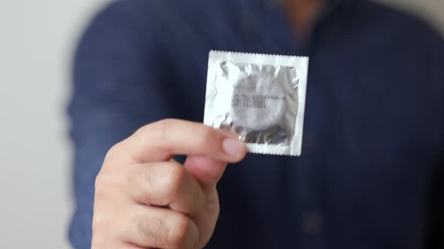 The young man showing the condom into camera. Campaign for safe sex and contraception. Close up male hand holding the condom.