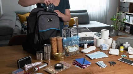 Unrecognizable woman putting cans of food to prepare emergency backpack in living room