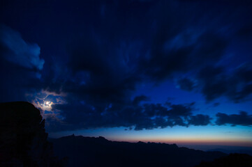 Moon with clouds in the blue hour over the swiss mountains 