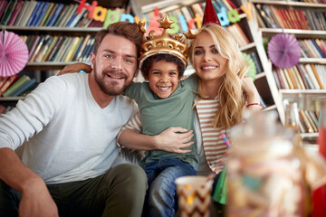 Happy couple enjoying a kids birthday party at home with their adopted son. Family, celebration, together