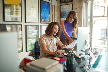  Good business relationship concept. Two caucasian young female colleagues enjoying their work, smiling.