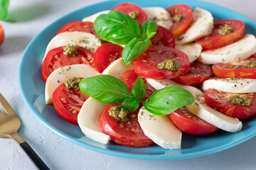 Italian caprese salad with sliced tomatoes, mozzarella cheese, basil and olive oil on a blue plate on light background. Close-up