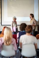 young caucasian male giving presentation to a group of people with his elderly female supervisor