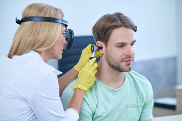 Doctor performing an otoscopic examination of the patients auditory canal - obrazy, fototapety, plakaty