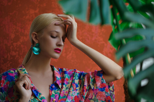 Elegant woman wearing trendy green shell earrings, colorful blouse, posing near orange wall. Summer fashion portrait. Copy, empty space for text