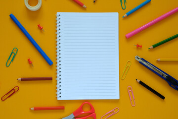 Flat lay. Yellow background. In the center lies a notebook on a spiral, around the stationery: paper clips, pencils, scissors. September 1, knowledge day, business.