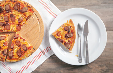Slice of pizza on plate, fork, knife on wooden table. Pizza on circle board
