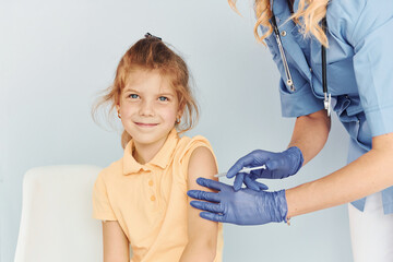 Little girl in yellow shirt. Doctor in uniform making vaccination to the patient