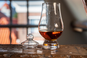 Dram of single malt scotch whisky served in tasting glass with view on old window and houses