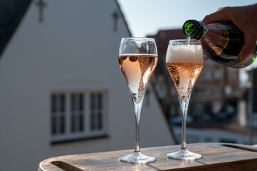 Pouring of rose champagne sparkling wine in flute glasses on outdoor terrace in France