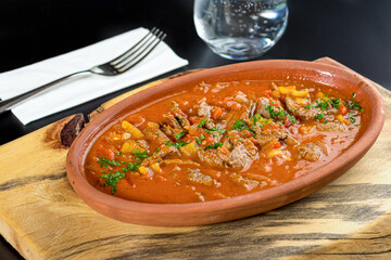 Meat sauteed in white casserole on black stone table