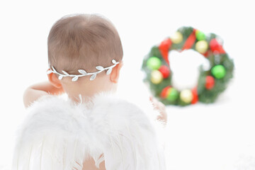 クリスマスリースを見つめる白い羽の赤ちゃん天使