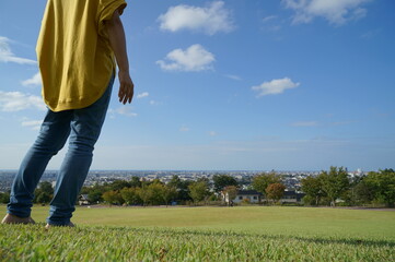 眺めの良い公園で青空のもと芝生の上で左側にいる頭から下の後ろ姿の1人の女性