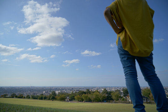 眺めの良い公園で青空のもと芝生の上で右側にいる頭から下の後ろ姿の1人の女性