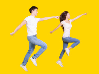 Fototapeta na wymiar Young couple jumping and pointing fingers on copyspace.Isolated over yellow background.