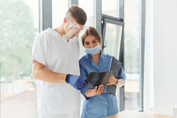 Obraz premium Looking at documents. Two doctors in uniform standing indoors and working together