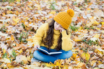 Reading really matters. Little child read book sitting on fall leaves. School library. Knowledge...