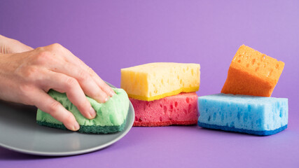 Dish cleaning with green sponge on violet background. Kitchen cleaning sponges. Set of colorful sponges for kitchen
