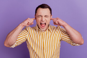 Portrait of crazy avoiding guy fingers cover ears shout close eyes on violet background