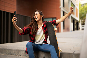 Fototapeta na wymiar Portrait of young beautiful girl with skateboard. Happy smiling woman taking selfie photo.