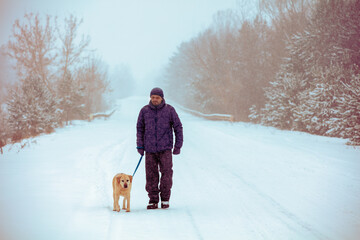 Fototapeta na wymiar A man and a dog are best friends. A man and a dog walk along a snowy country road at blizzard