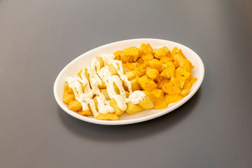 Mixed portion of fried potatoes with brava sauce and garlic mayonnaise sauce on a white tray