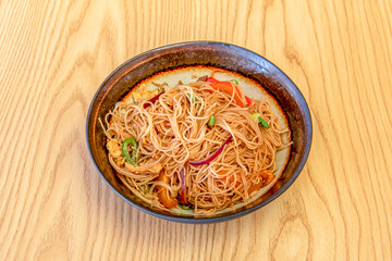 nice bowl of rice noodles with wok-sautéed vegetables, chicken pieces and red onion on light wooden table
