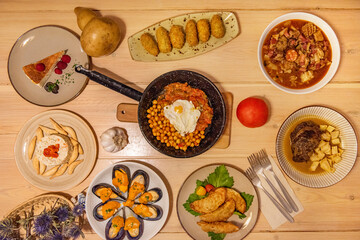 Top view image of popular Spanish food dishes. Chickpea stew with egg and ratatouille, Madrid-style tripe, cheek with fried potatoes, steamed Galician mussels, Russian salad