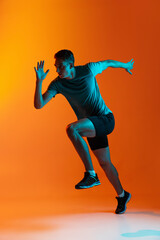 Fototapeta na wymiar Portrat of Caucasian professional male athlete, runner training isolated on orange studio background with blue neon filter, light. Muscular, sportive man.