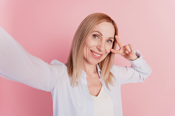 Attractive young woman happy positive smile shows peace v-sign sign make selfie on isolated pink background