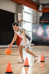 Fototapeta premium Tattoed man in white shportswear playing basket-ball and looking involved