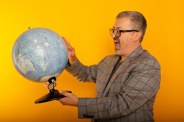An adult puzzled man with glasses on a yellow background holds a globe in his hand.
A teacher at...