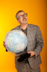 An adult puzzled man with glasses on a yellow background holds a globe in his hand.
A teacher at the school teaches students geography. Knowledge day.