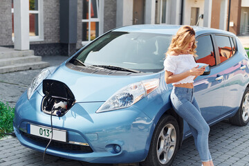 Standing near the car. Young woman in casual clothes with her electromobile outdoors at daytime