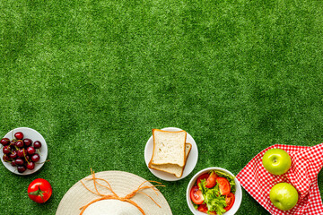 Picnic basket with red tablecloth on the garden green grass. Top view