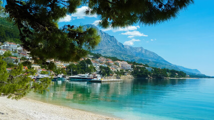 Brela, Croatia - May 9. 2014: View beyond pine tree branches over bay in adriatic sea on hill with village, blurred dizzy mountain background (Focus on center of village)