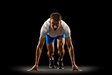 Obraz premium Sportive young man, male athlete, runner training isolated on dark studio background with spotlight. Concept of action, motion, youth, healthy lifestyle.