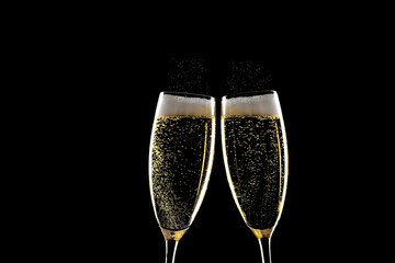 Two glasses of champagne with spray above over black background