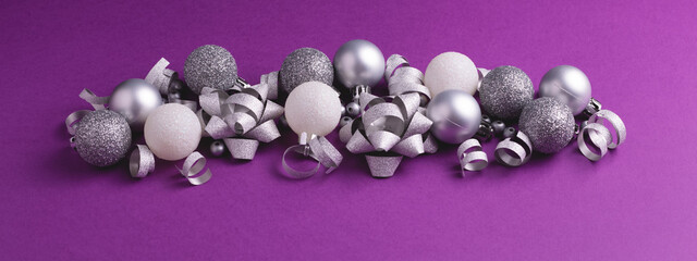 Christmas and New Year ornament on purple background. Silver and white metallic baubles and bows. Banner 16:6