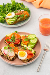 Healthy tasty breakfast, sandwiches with avocado and salmon, cucumbers and tomatoes, radishes and microgreens of peas with boiled egg and root salad, grapefruit smoothie in a glass