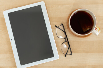 Fototapeta na wymiar Tablet, eyeglasses and tea cup on wooden office desk.