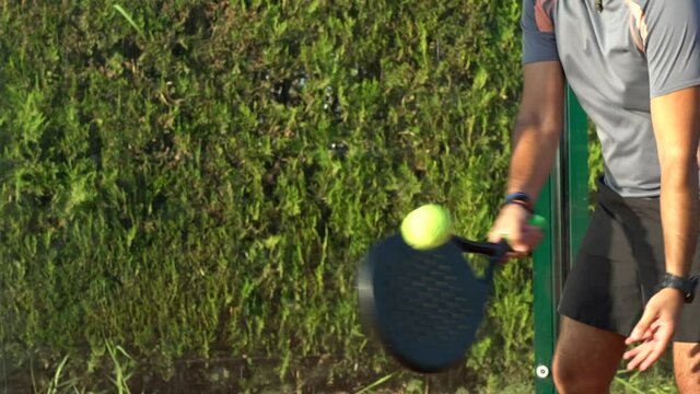 Slow motion of a male paddle tennis player hitting the ball during a match on an outdoor court. View from bottom to top.