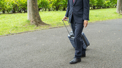 スーツケースを引っ張るビジネスマン。遊歩道を歩く男性。
