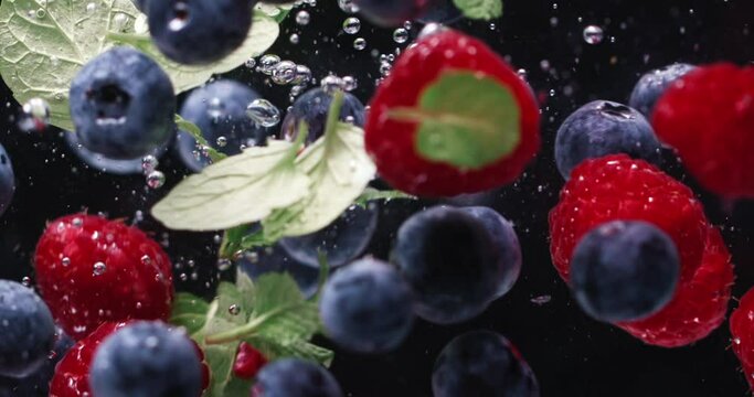 Fresh Blueberry, Raspberry, and Mint Splashing into the Clear Water. Colorful Berries falling slowly in water with bubbles on Dark Background. Summer Fruits. Healthy Food. Vitamins.